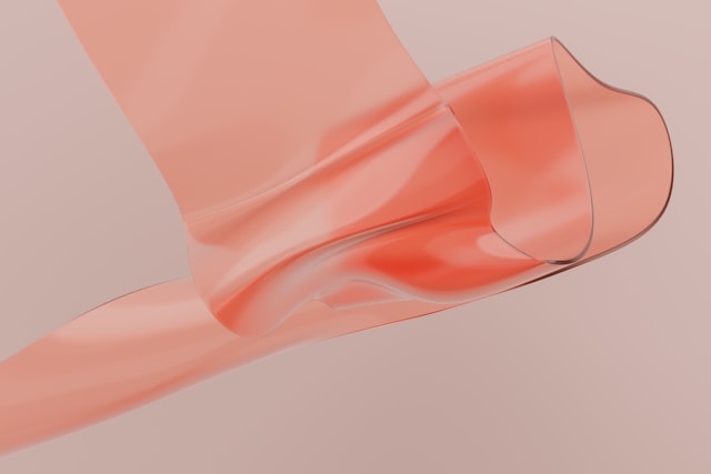 A translucent coral-colored ribbon or fabric flowing gracefully against a soft pink background.